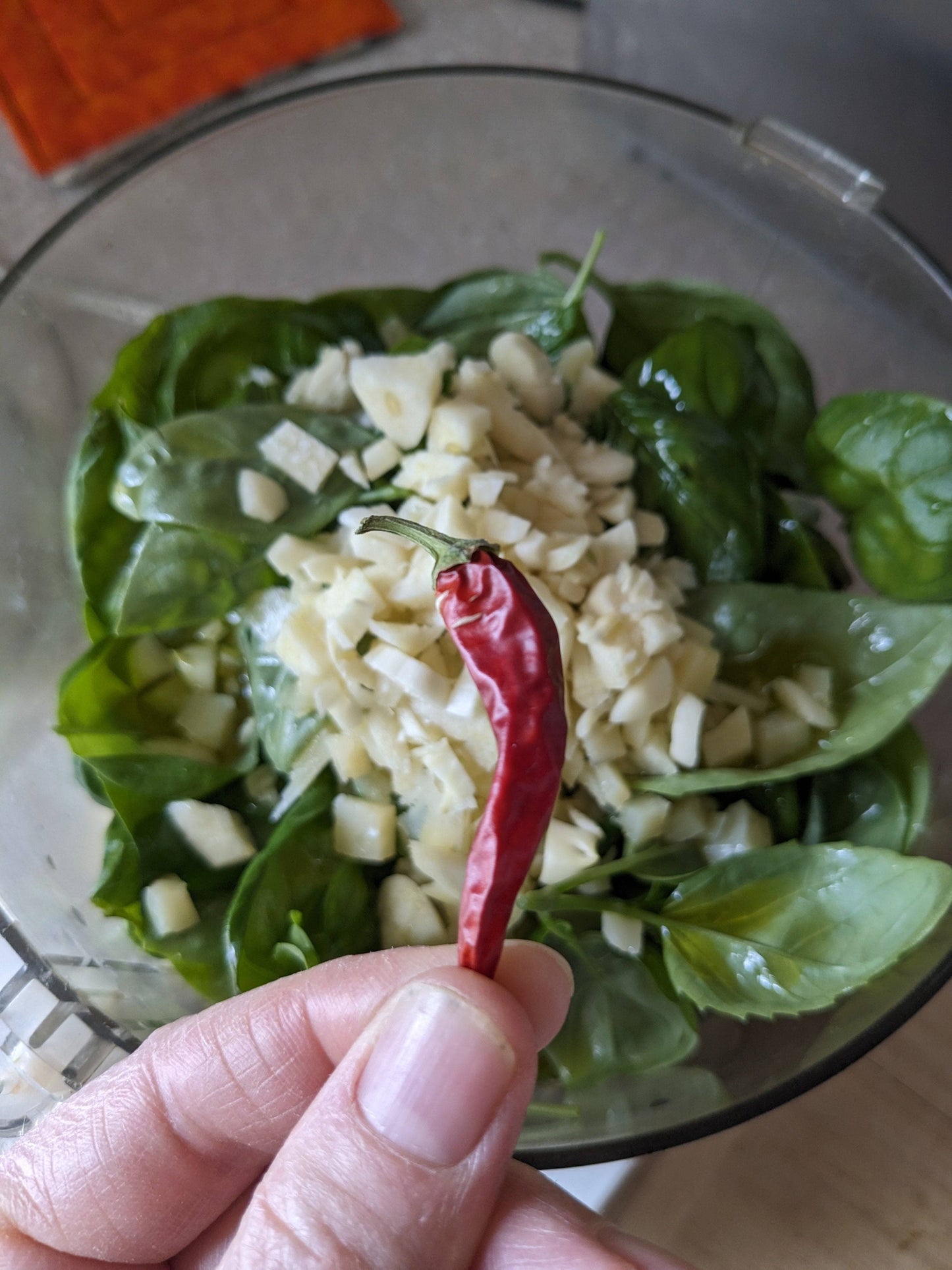 Fresh Basil Genovese leaves with garlic and chili pepper in a food processor. Ingredients ready for making homemade pesto or Italian dishes.