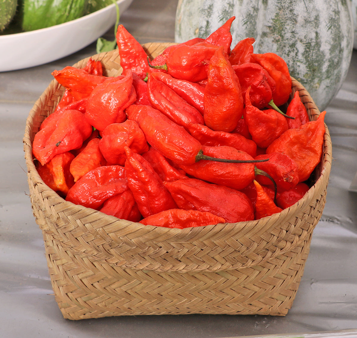 Basket filled with freshly harvested red Naga Morich peppers, ideal for gardeners seeking super hot heirloom chili varieties.