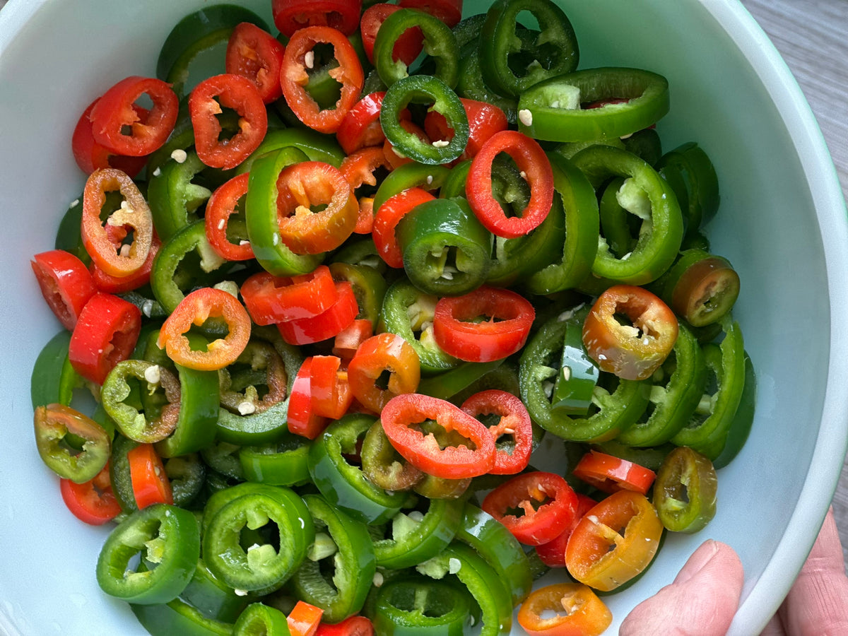 Sliced green and red jalapeño peppers in a white bowl.