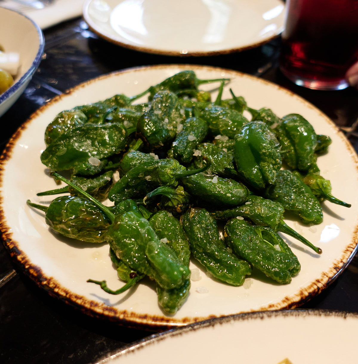 Cooked Padron peppers served on a plate with sea salt, showcasing the gourmet sweet heirloom flavor ideal for homegrown culinary use.