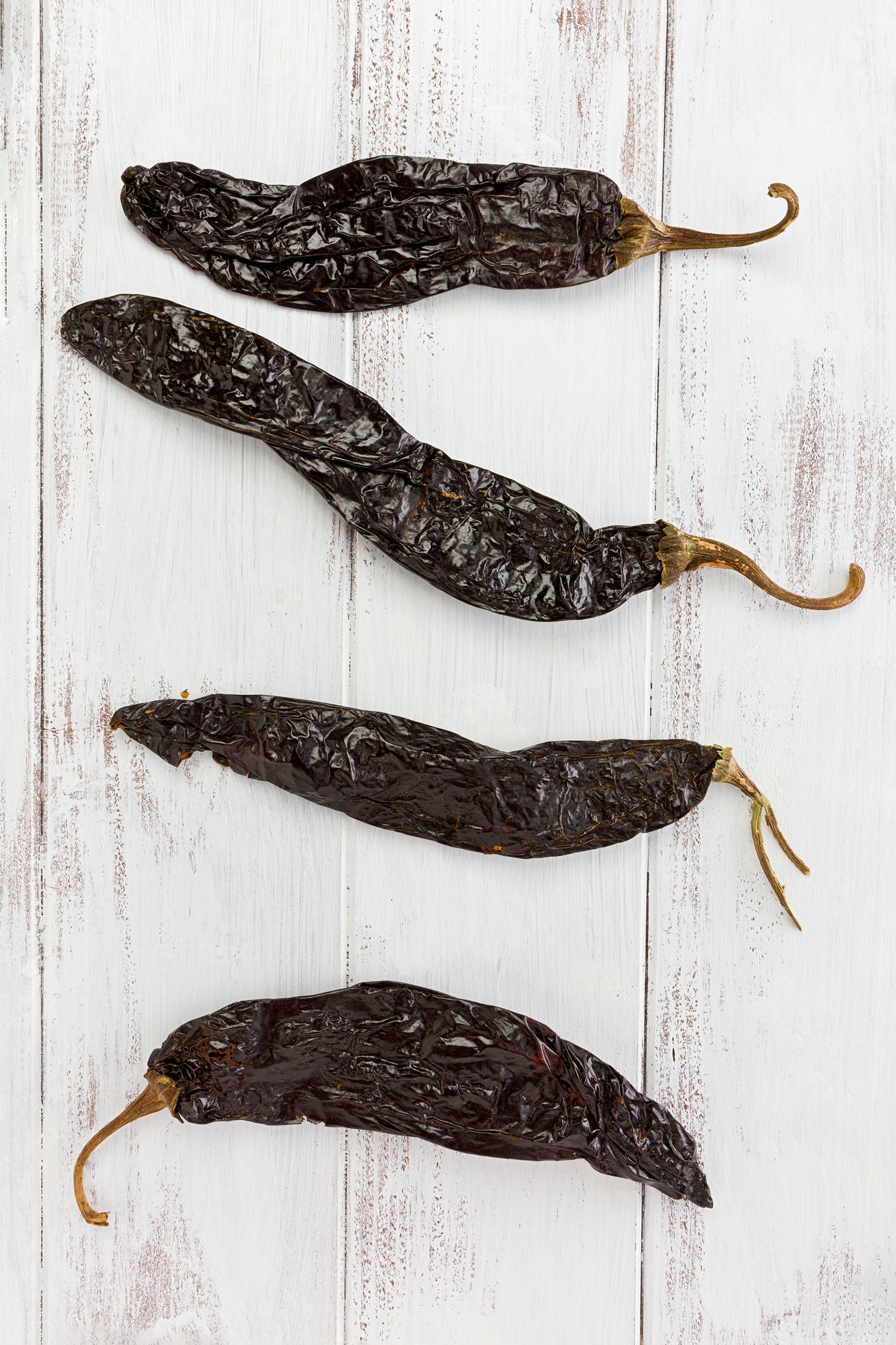 Dried Pasilla Bajio/Chilaca chiles with wrinkled dark skin, commonly used in mole sauces and traditional Mexican dishes for rich, mild flavor.