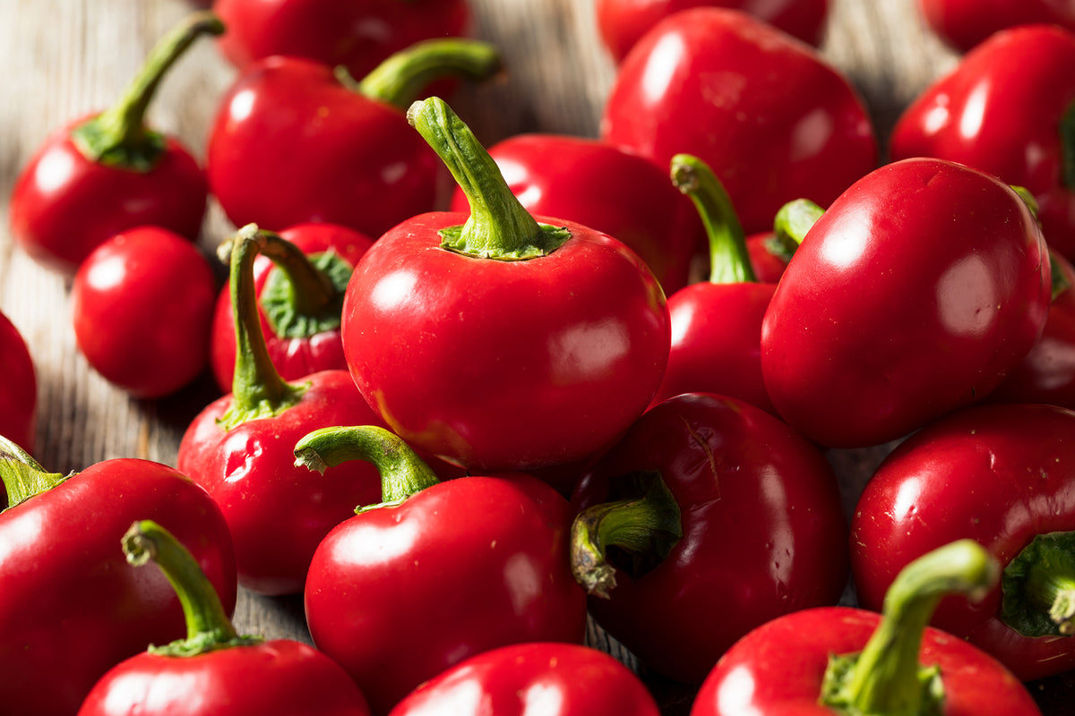 Close-up of hot red cherry peppers with green stems on a wooden surface