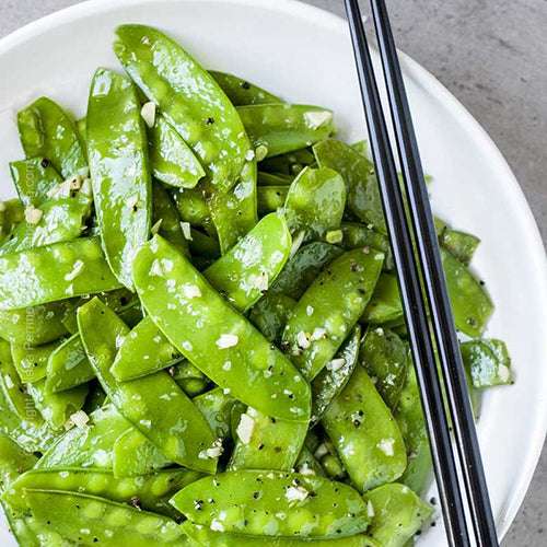 Cooked Oregon Sugar Pod peas in a white bowl with garlic and seasoning. Great for stir-fries and healthy vegetable dishes.