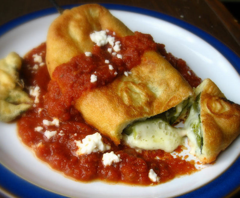 Stuffed poblano pepper relleno topped with red sauce and cheese, showcasing culinary use of mild heirloom poblano peppers.