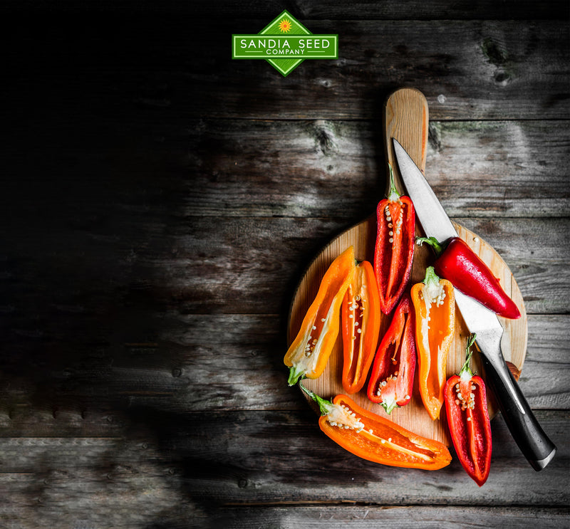 Pepper Pop Quiz! A colorful array of sliced red, orange, and yellow bell peppers with seeds, arranged on a wooden cutting board on a rustic dark wood surface, illustrating fresh vegetable preparation for cooking or gardening.