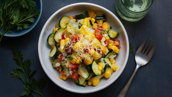 A colorful calabacitas recipe salad with zucchini, corn, cherry tomatoes, and cheese, served in a white bowl on a dark surface.