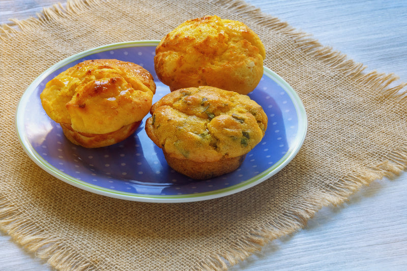 Colorful Chile Cornbread muffins on a blue and white dotted plate, showcasing golden-brown crusts and spicy chili ingredients, perfect for Southern or Mexican cuisine.