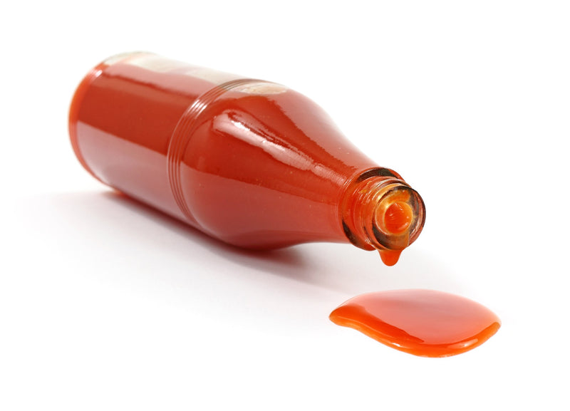 A bottle of vibrant red Louisiana hot sauce spilling onto a white surface, highlighting its spicy, tangy flavor profile.