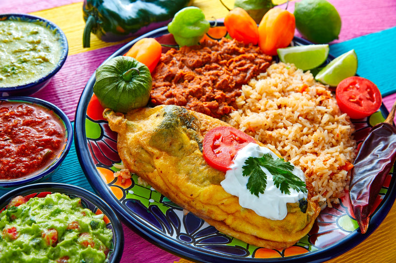 Colorful Mexican homegrown chile relleno dish with rice, fresh vegetables, and traditional sauces on a vibrant table, showcasing authentic Mexican cuisine.