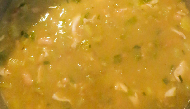 Close-up of a simmering pot of roasted green chile chicken soup with a rich, flavorful broth, green chile pieces, and shredded chicken.