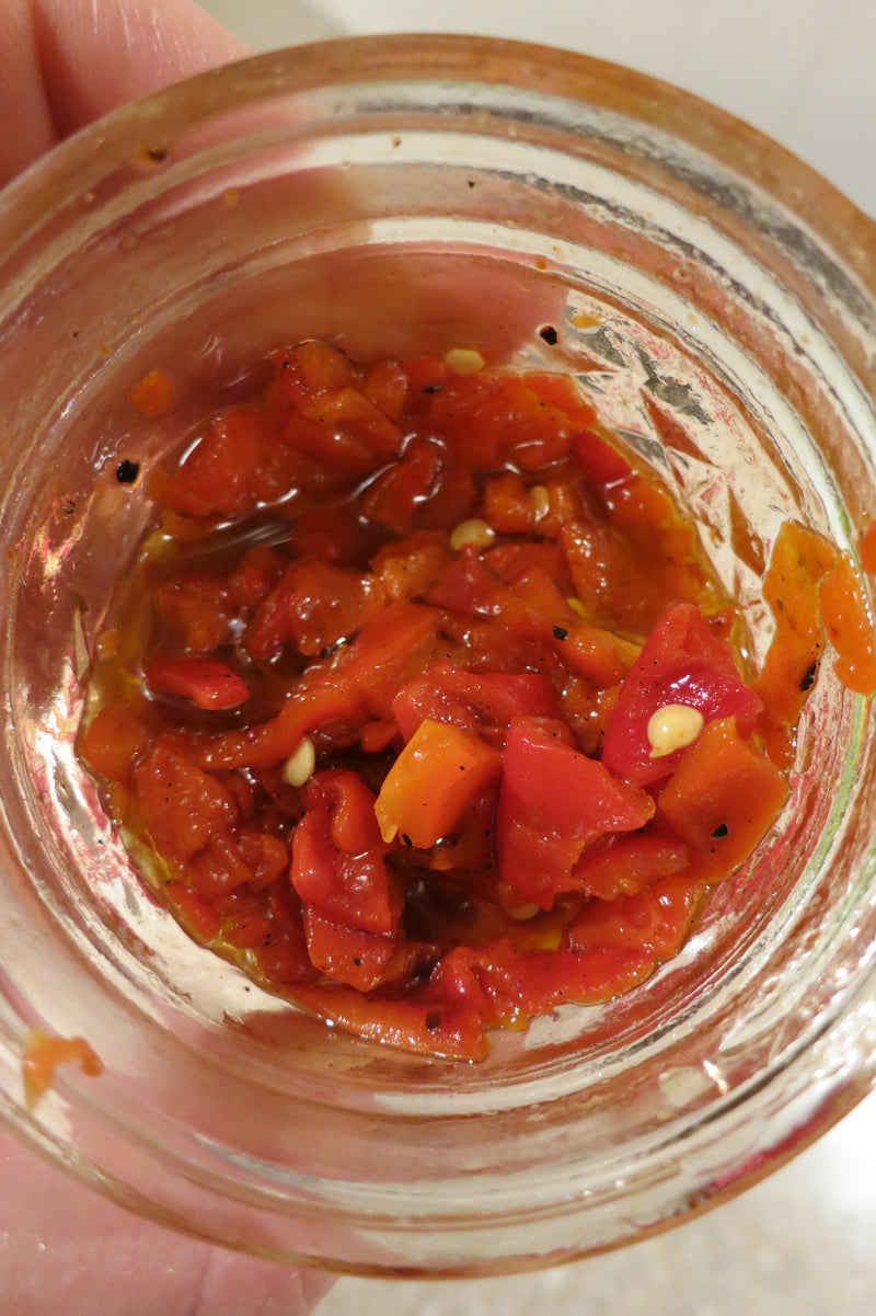 Homemade Marinated Piquillo Peppers Recipe: A glass jar containing homemade marinated piquillo peppers with a vibrant red color, immersed in a flavorful marinade with visible garlic and spices.
