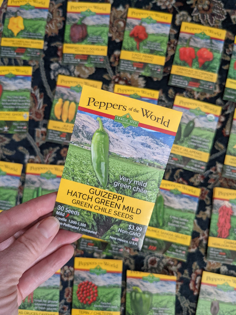 Pepper Seeds from Sandia Seed: A packet of pepper seeds labeled Guizeppi Hatch Green Mild Green Chile Seeds with background of other pepper seed packets, held in a person's hand.