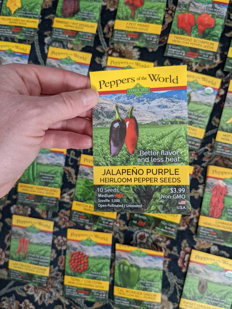 A close-up of a pepper seed packet labeledJalapeño Purple" from Peppers of the World, featuring colorful peppers and scenic landscape, ideal for buying heirloom pepper seeds.