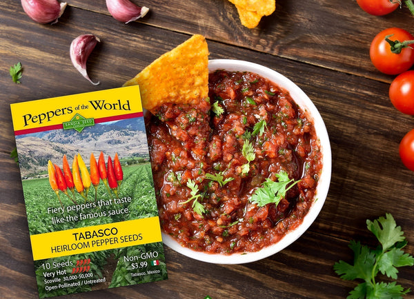 Tabasco Pepper Salsa Recipe - Bowl of salsa with Tabasco Seed Packet from Sandia Seed with salsa ingredients on wooden table with cilantro, tomatoes and garlic