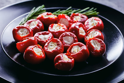 Stuffed sweet red cherry peppers arranged on a black plate with a sprig of rosemary garnish, photographed in a dark studio setting.
