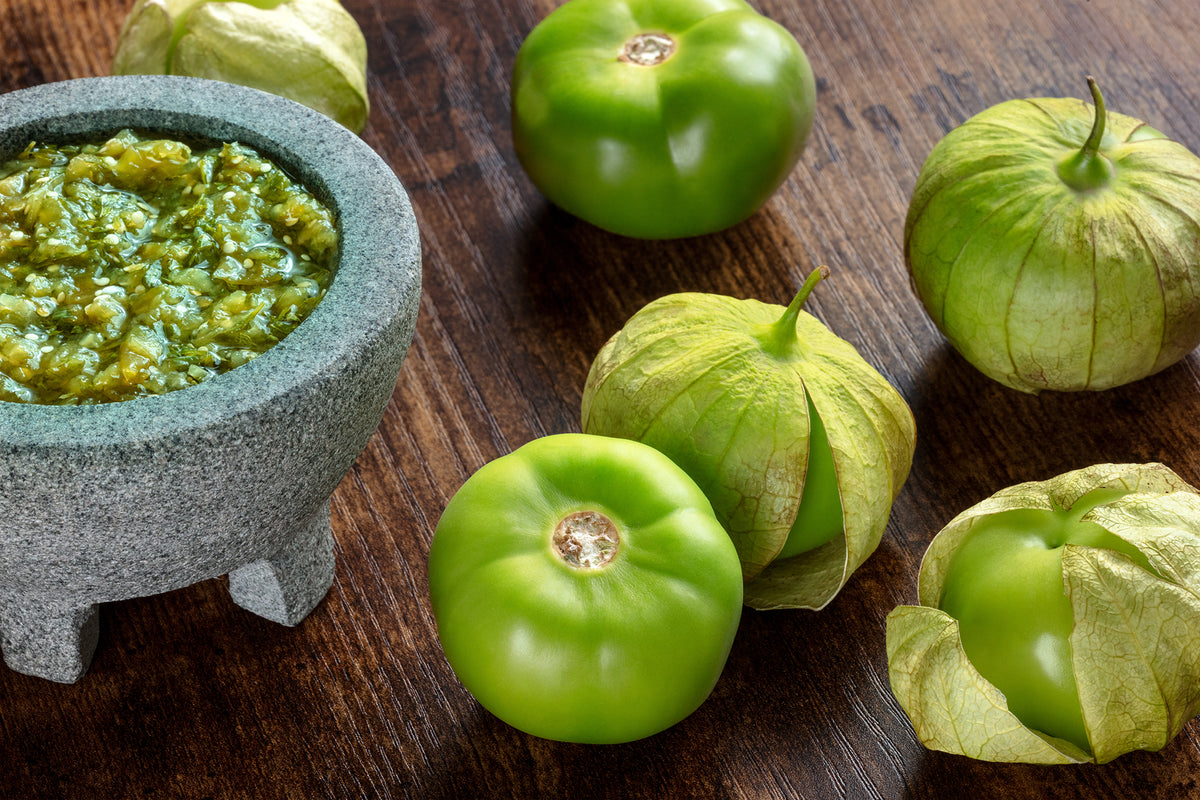 Green tomatillos and a mortar with green salsa on a wooden surface